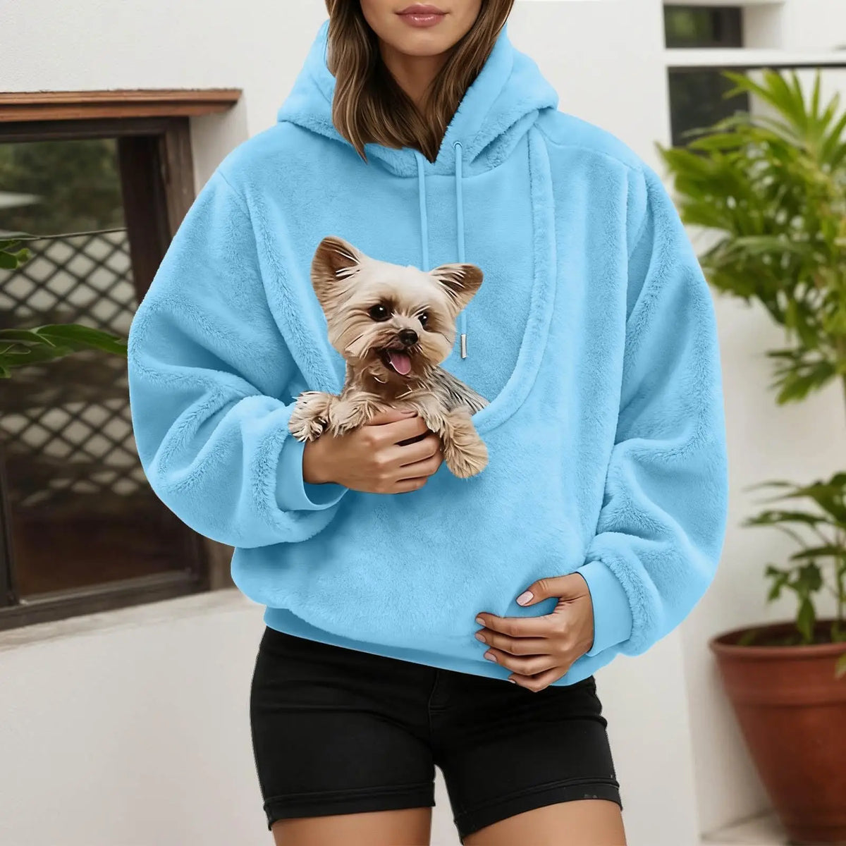 Person wearing the sky blue fleece pouch hoodie with a small terrier held in the front pouch